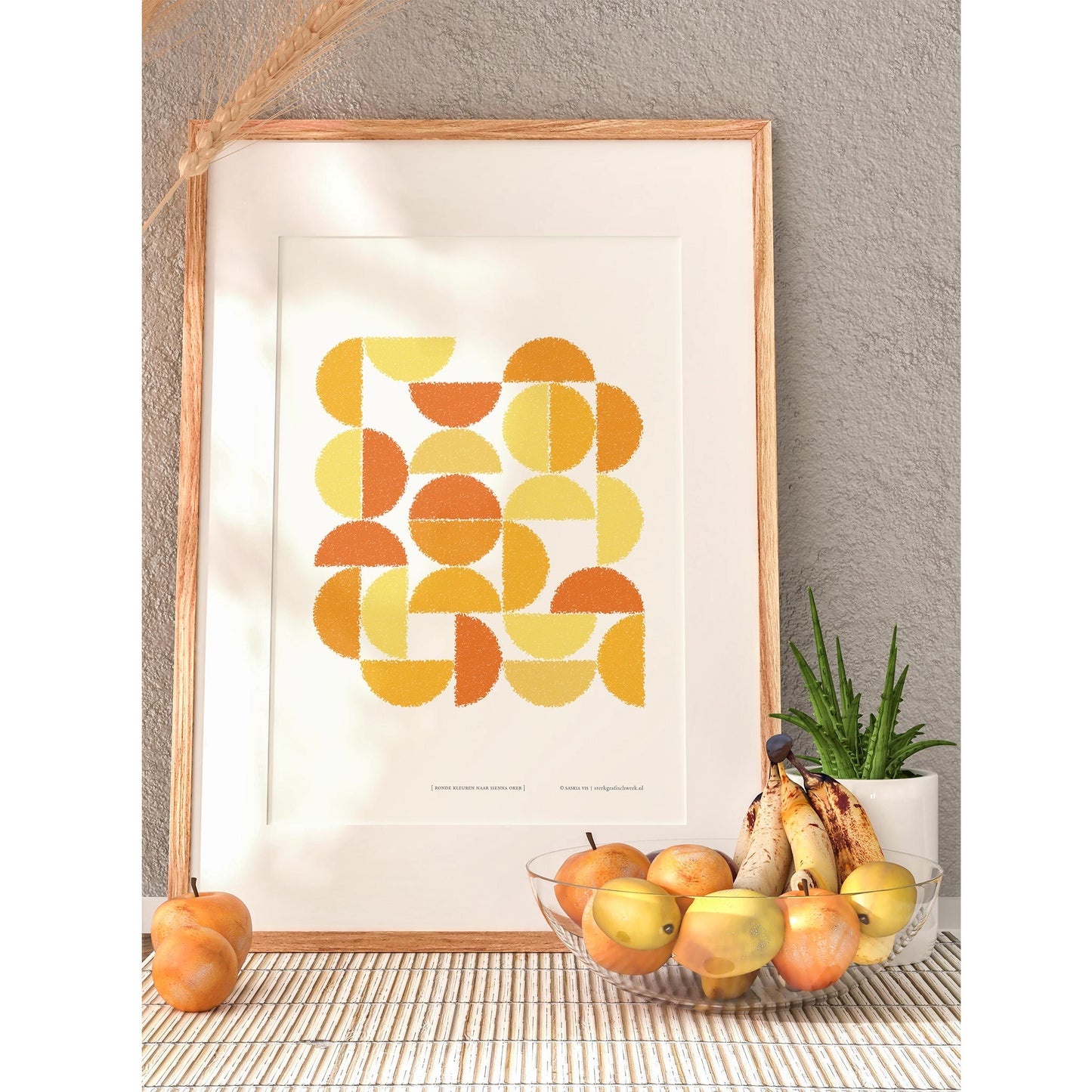 Productafbeelding, poster "ronde kleuren naar sienna oker", in een houten lijst met een schaal en wat fruit erbij, ter impressie