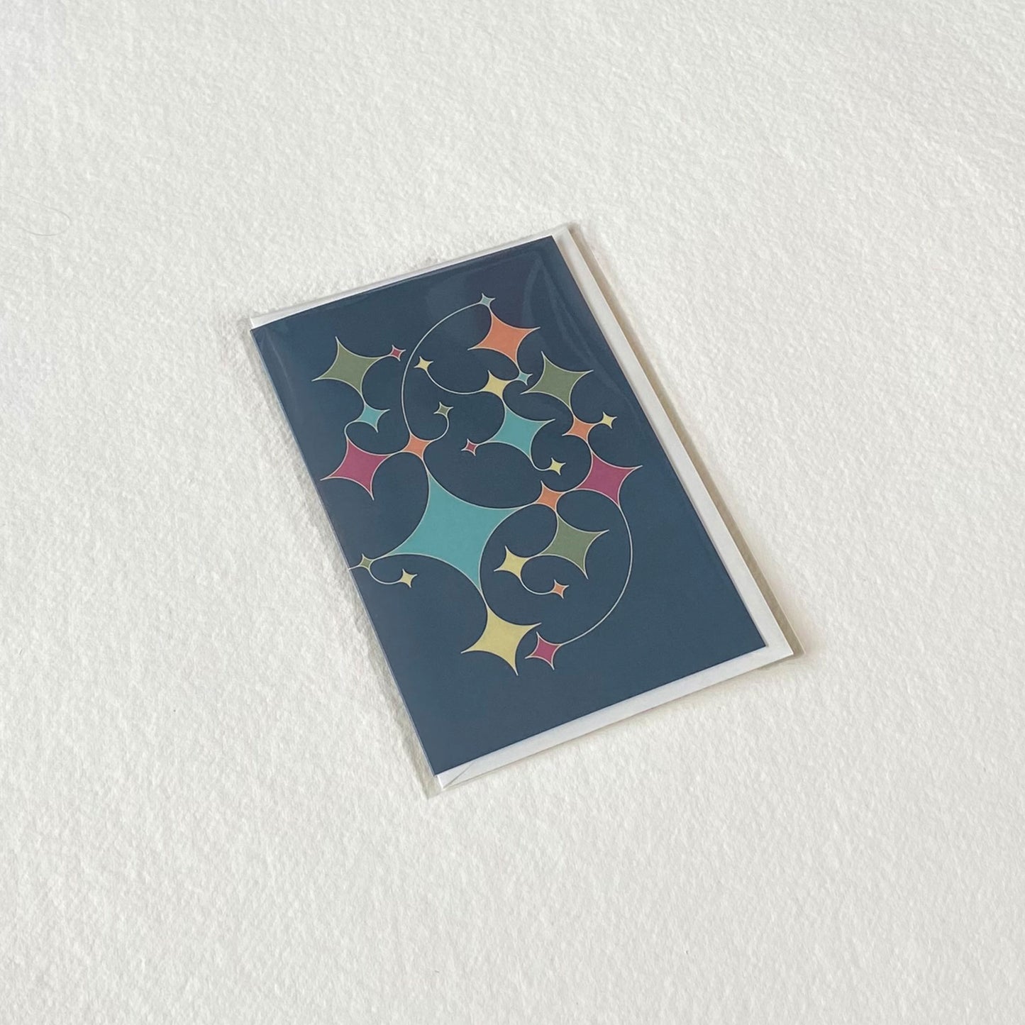 Productafbeelding, foto wenskaart "rising stars (blauw)" in zijn verpakking liggend op een achtergrond