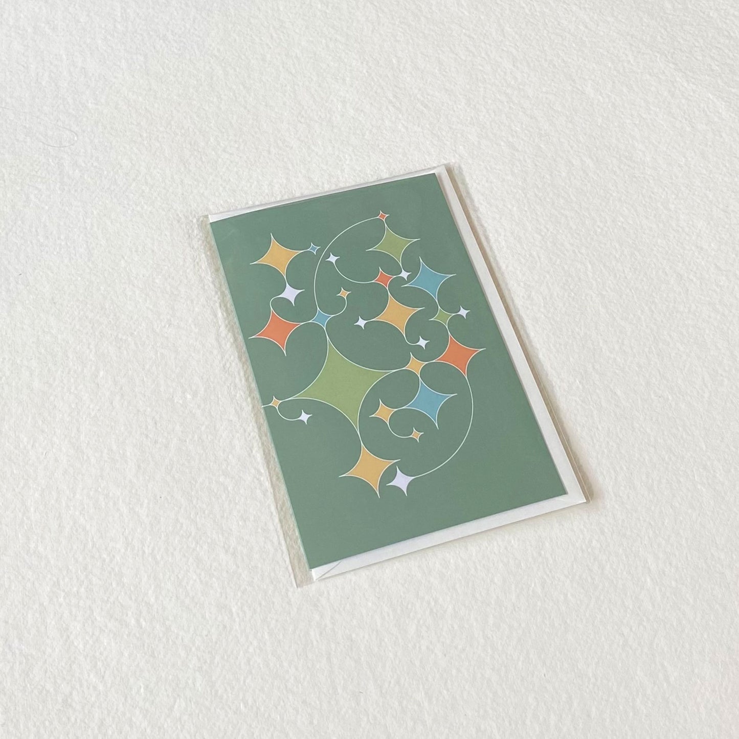 Productafbeelding, foto wenskaart "rising stars (donkergroen)" in zijn verpakking liggend op een achtergrond