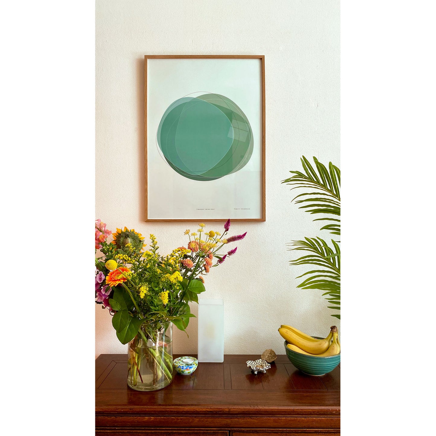 Productafbeelding, poster "vorm zeven in vert-blue océan", ingelijst aan een wand boven een wandtafel met bloemen, fruit en wat decoratie