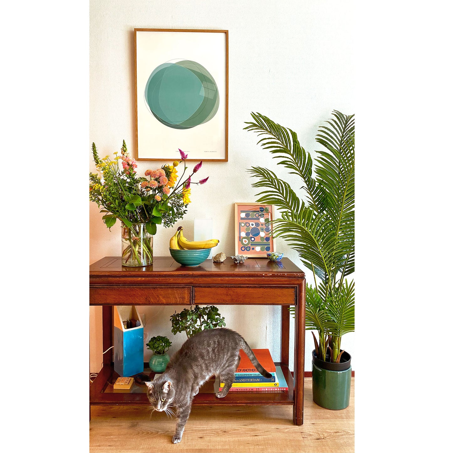 Productafbeelding, poster "vorm zeven in vert-blue océan", een sfeerfoto hangend in een interieur met een plant, een wandtafel, een kat en nog meer interieur decoratie