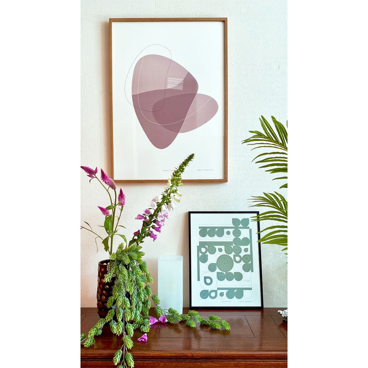 Productafbeelding, poster "vorm acht in aubergine", een sfeerfoto, ingelijst boven een side-table met bloemen, planten en nog en kleine ingelijste andere poster
