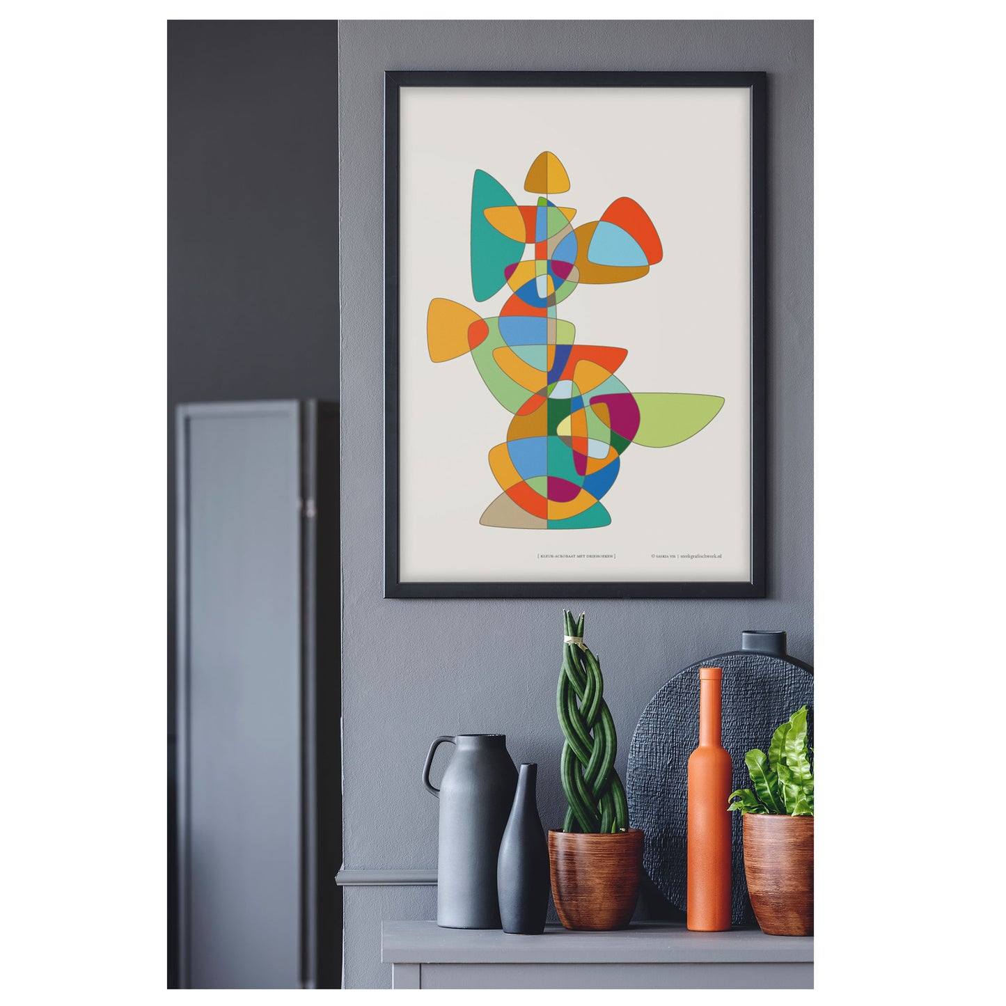 Productafbeelding, poster "kleur-acrobaat met driehoeken" foto impressie 2, hangend in een grijskleurig interieur