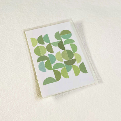Productafbeelding, foto wenskaart "ronde kleuren naar bladgroen" in zijn verpakking liggend op een achtergrond