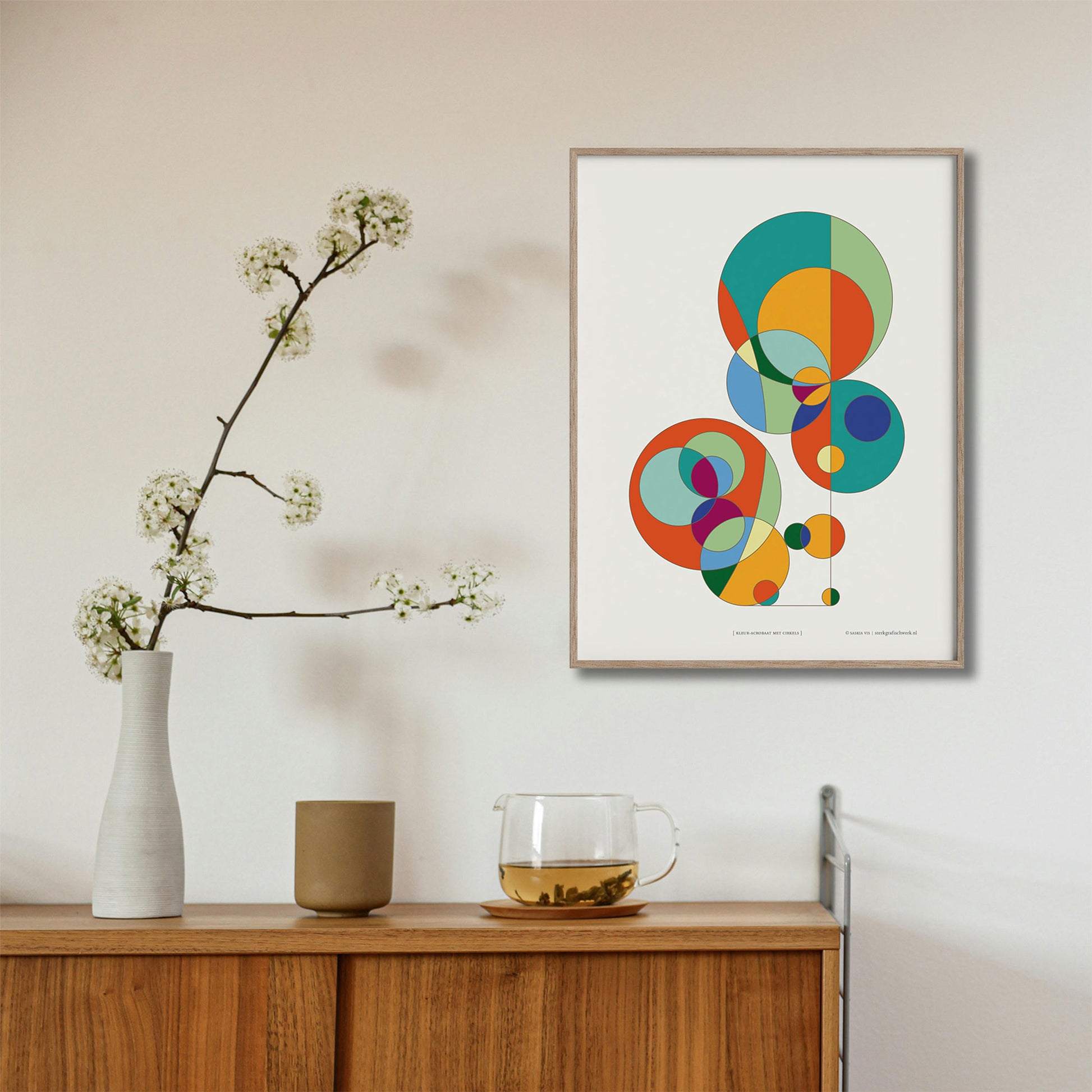 Productafbeelding, poster "kleur-acrobaat met cirkels", foto impressie 3, hangend in een houten lijst boven een side-table. 