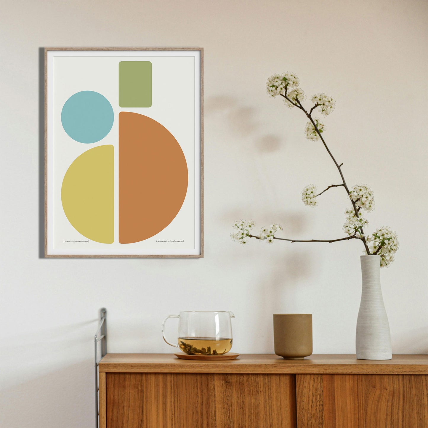 Productafbeelding, poster "een gekleurde ronde som", foto impressie 4, ingelijst in een houten lijst boven een side-table.