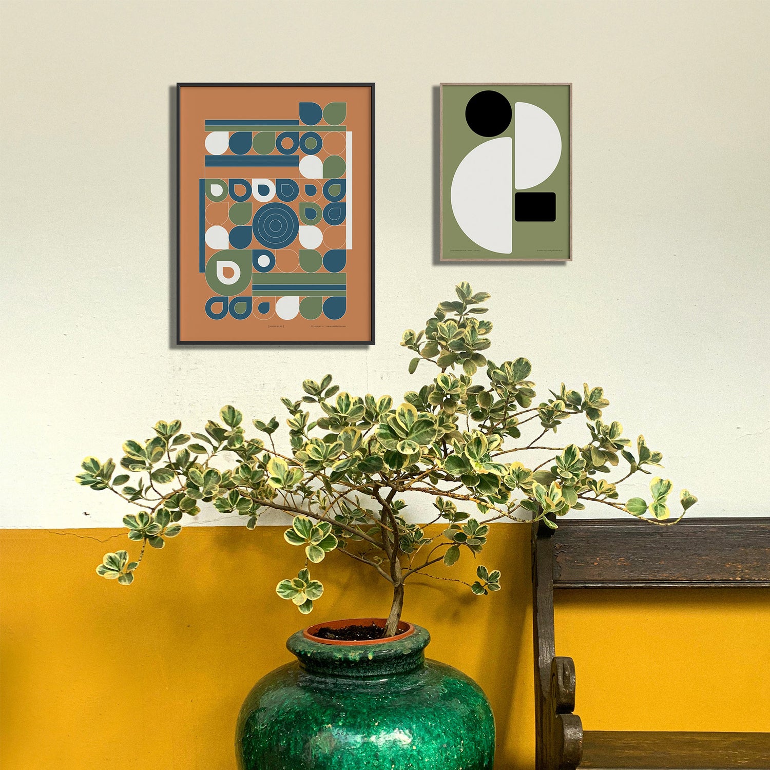 Twee ingelijste posters aan een wand met een plant en een houten bankje, een sfeerfoto